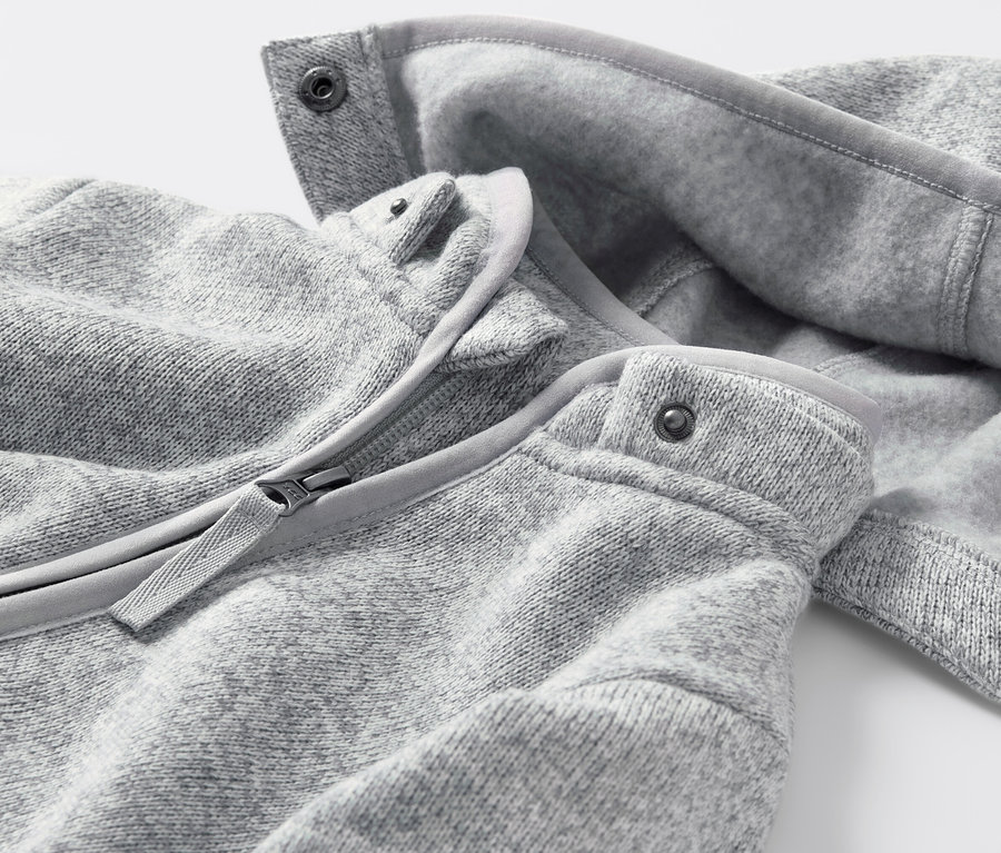 Detail dětského overalu z pleteného fleecu se zipem a patentkami.