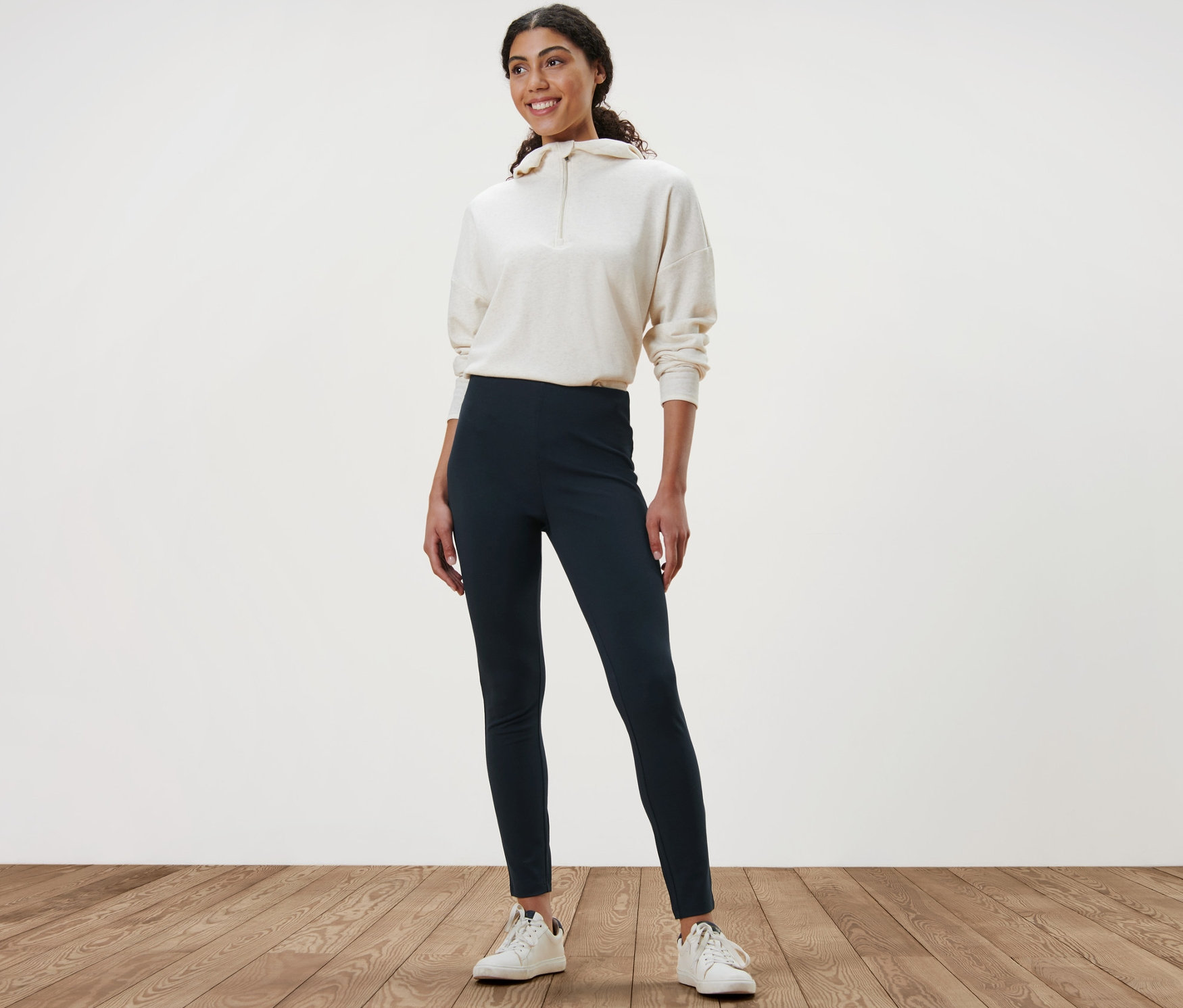 Žena stojící na dřevěné podlaze má na sobě hrubé legíny a mikinu.