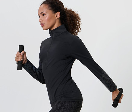 Žena v černém sportovním oblečení drží v každé ruce běžecké a gymnastické činky.