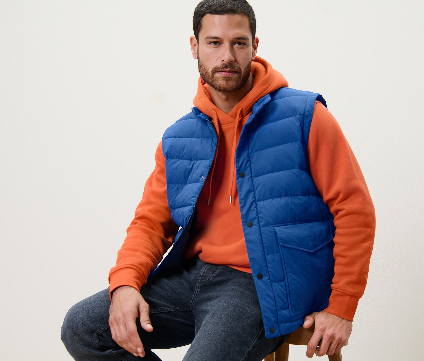 Muž sedí na stoličce v modré prošívané vestě.