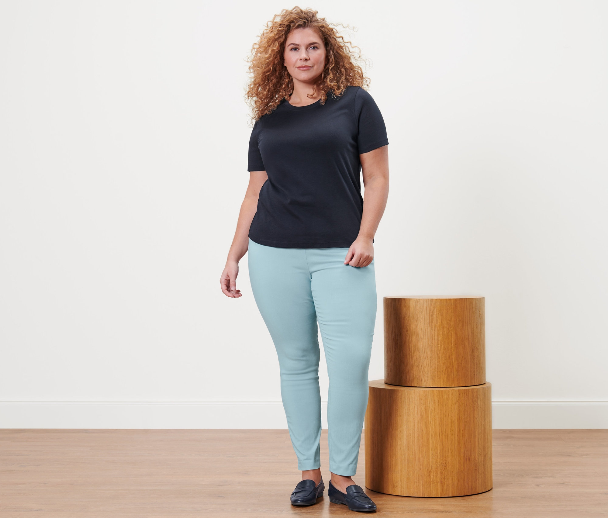 Žena stojí a má na sobě tmavě modré tričko Basic, strečové kalhoty a kožené mokasíny.