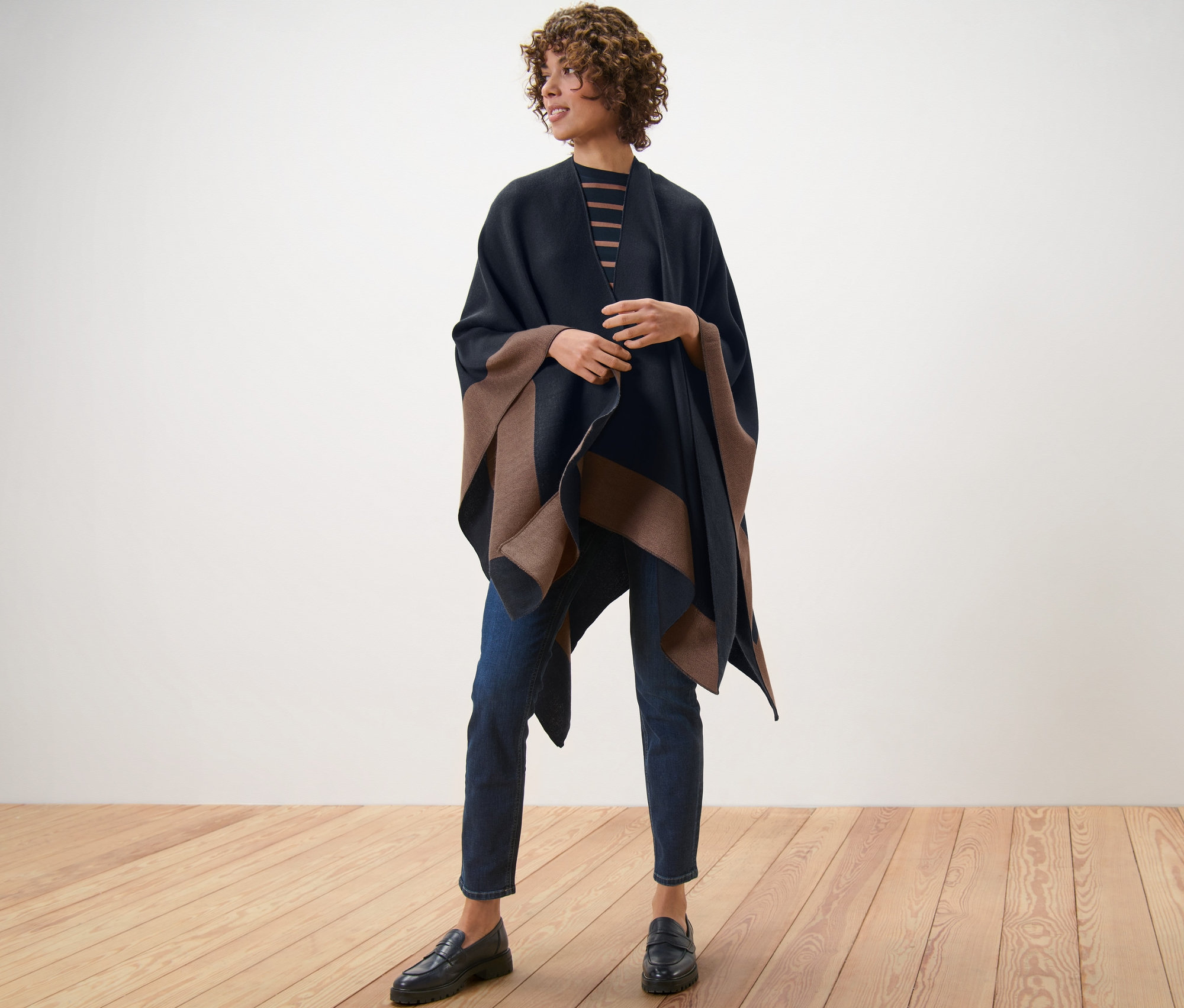 Žena stojící na dřevěné podlaze má na sobě oboustranné pončo.