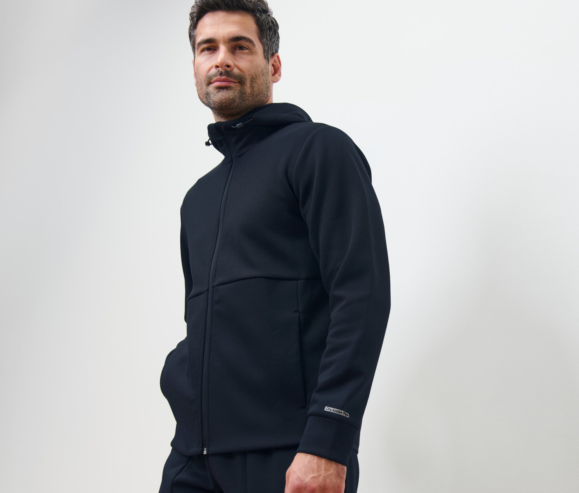 Muž pózuje v tmavě modré funkční mikině.