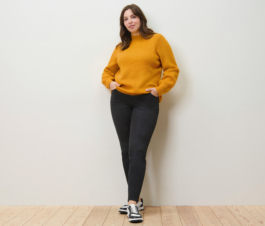 Žena pózuje v svetru z hrubého úpletu a džínách slim fit »Emma«.