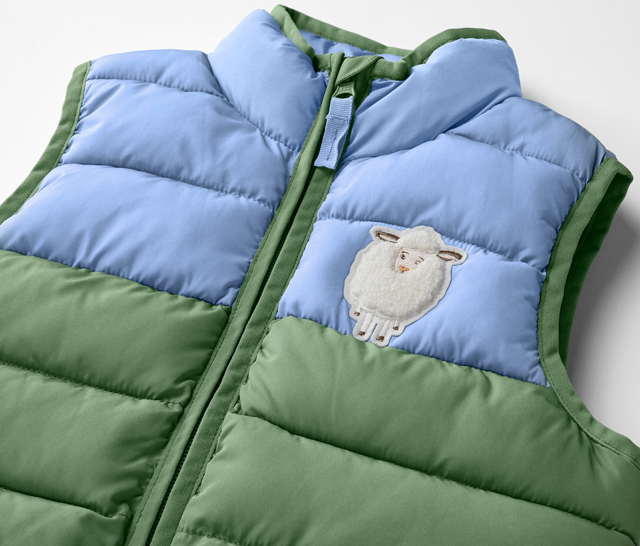 Detail dětské prošívané vesty, color blocking, s nášivkou ovečky.