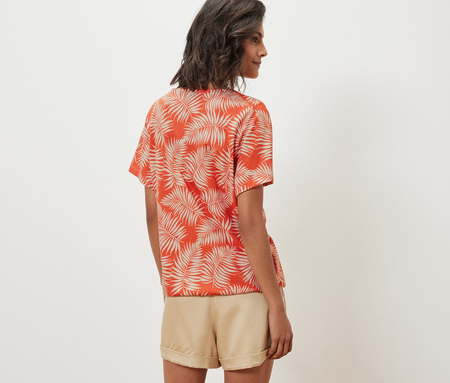 Žena má na sobě halenkové triko s potiskem a šortky.