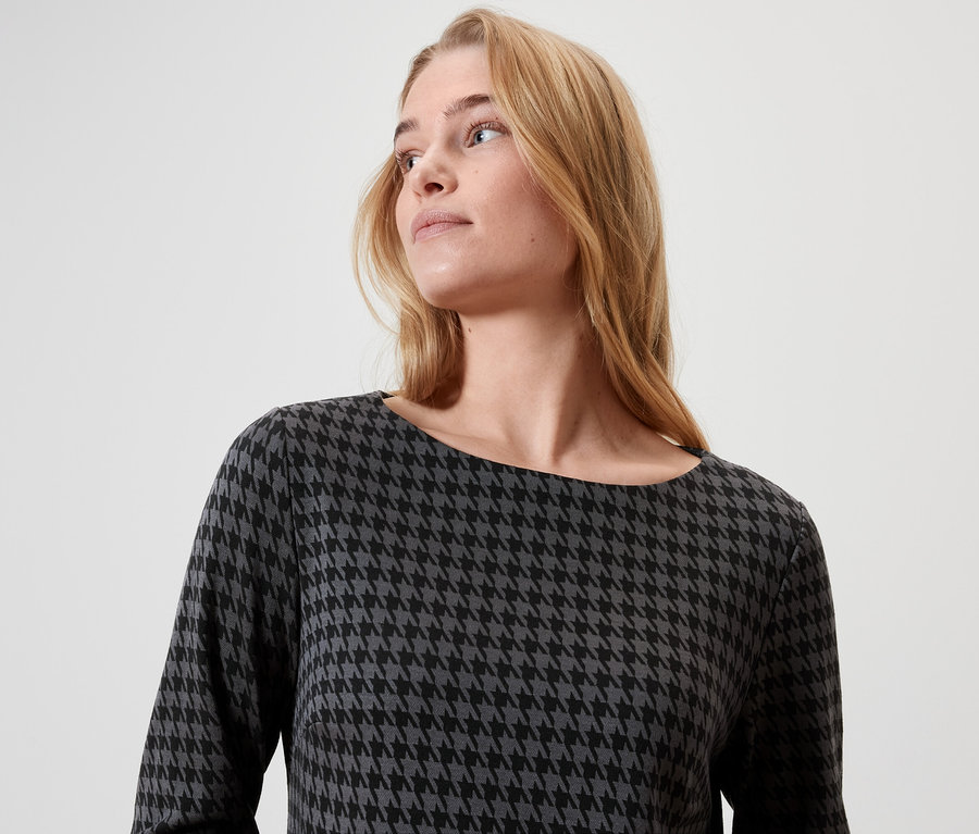 Blondýna s dlouhými vlasy má na sobě šaty s kohoutí stopou.