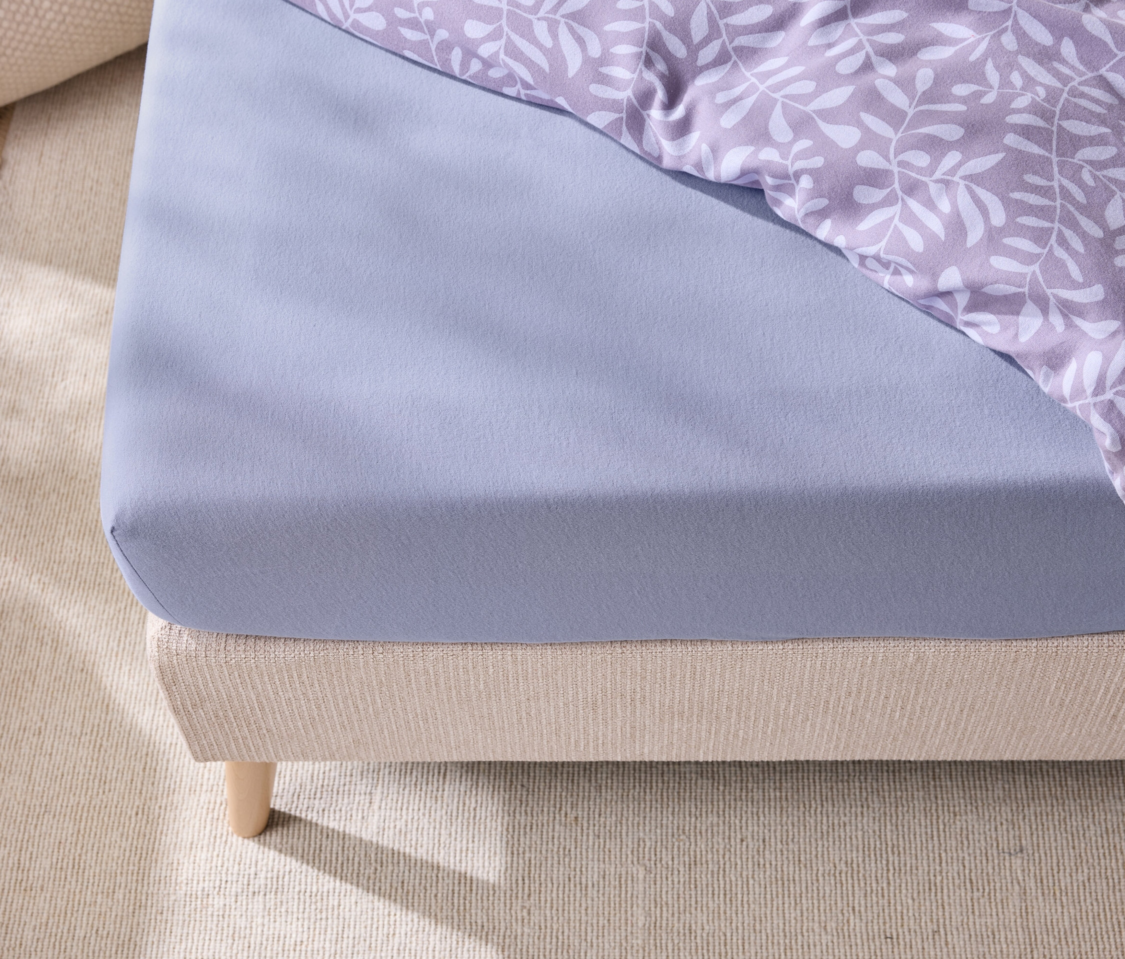 Detail modrého prostěradla a povlečení s lístky na posteli.