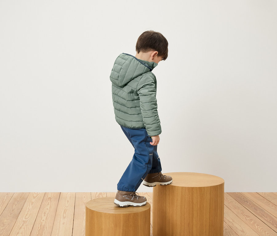 Chlapec v zelené bundě a modrých kalhotách stoupá na dřevěný podstavec.