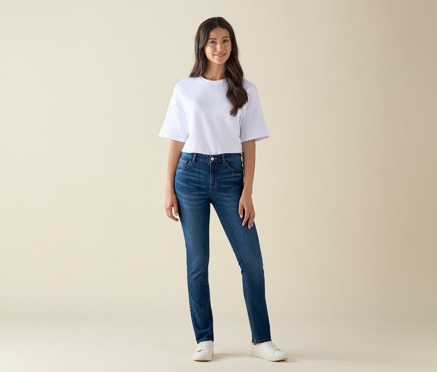 Žena stojí a má na sobě džíny slim střihu »Emma« v mid blue denim a bílé tričko.