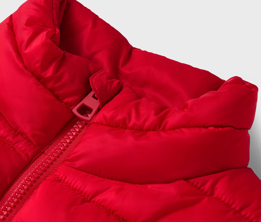Detail červené prošívané vesty s červeným zipem.