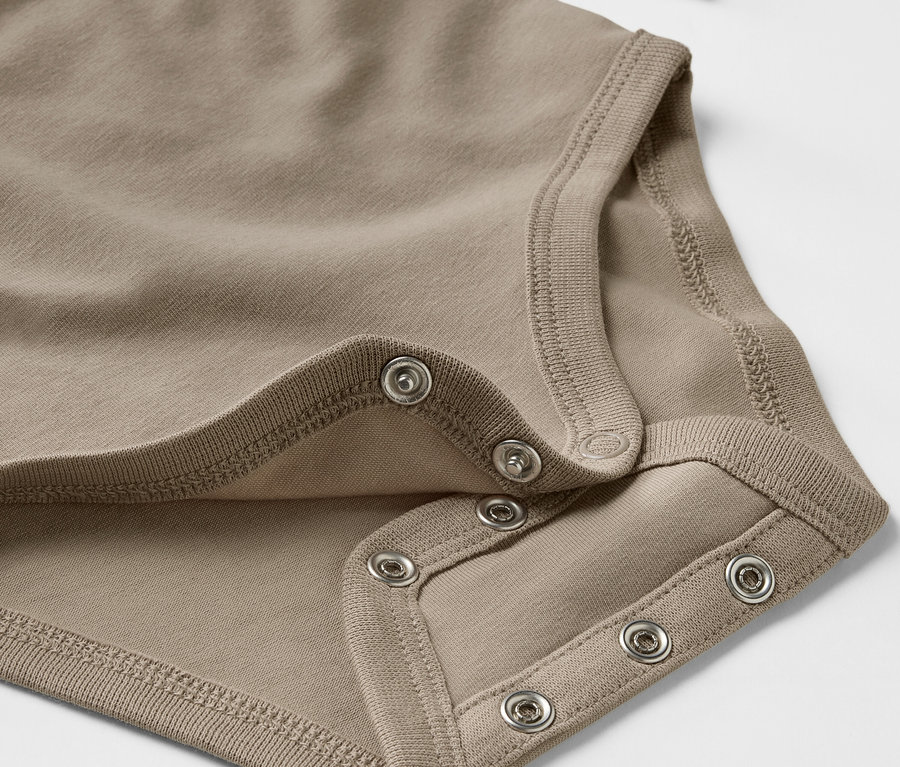 Detail hnědého rostoucího body pro miminka s patentkami.