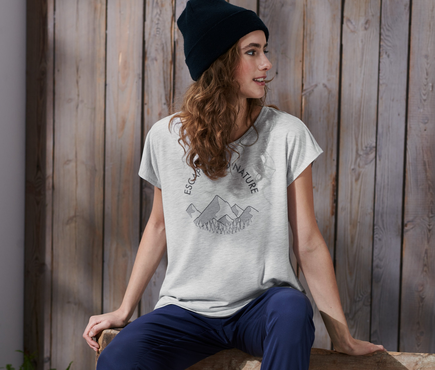 Žena sedí na lavičce a má na sobě šedé funkční triko s potiskem.