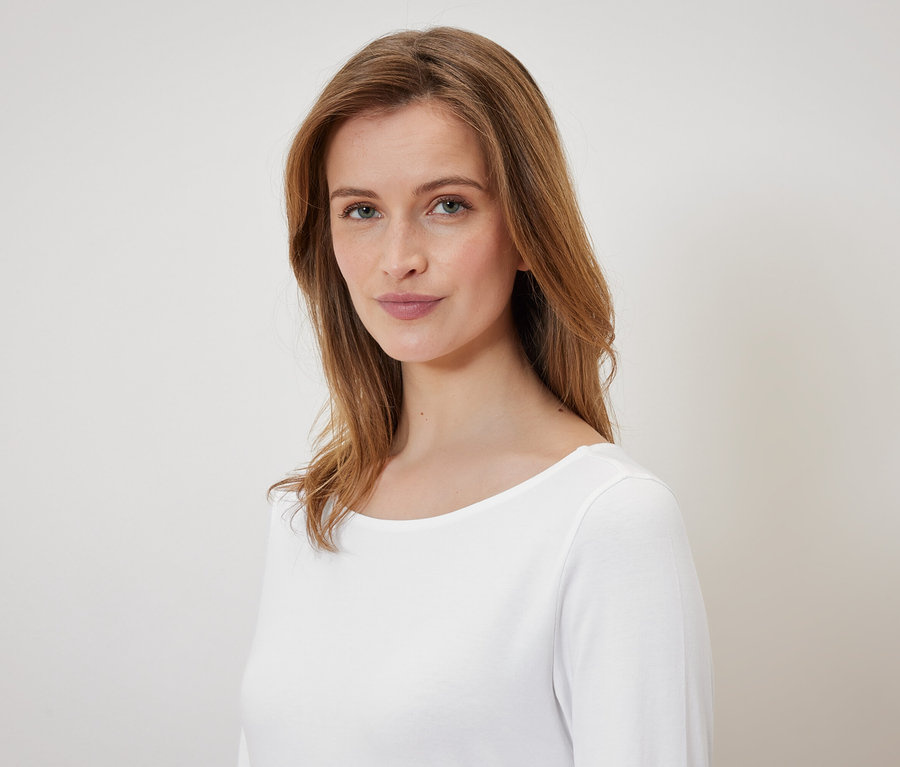 Portrét ženy s hnědými vlasy a modrýma očima v bílém tričku.