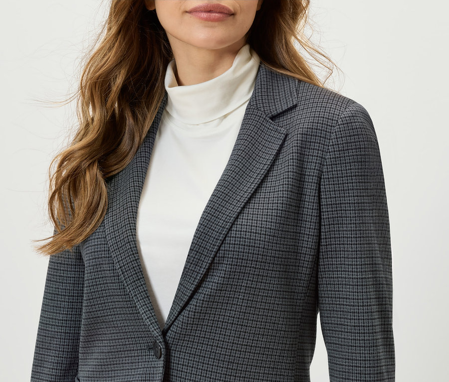 Žena má na sobě kostkované sako a bílý rolák.