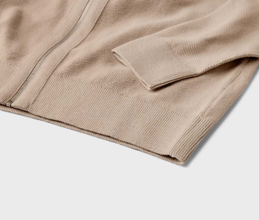 Detail béžového pleteného svetru na zip s žebrovanými manžetami.