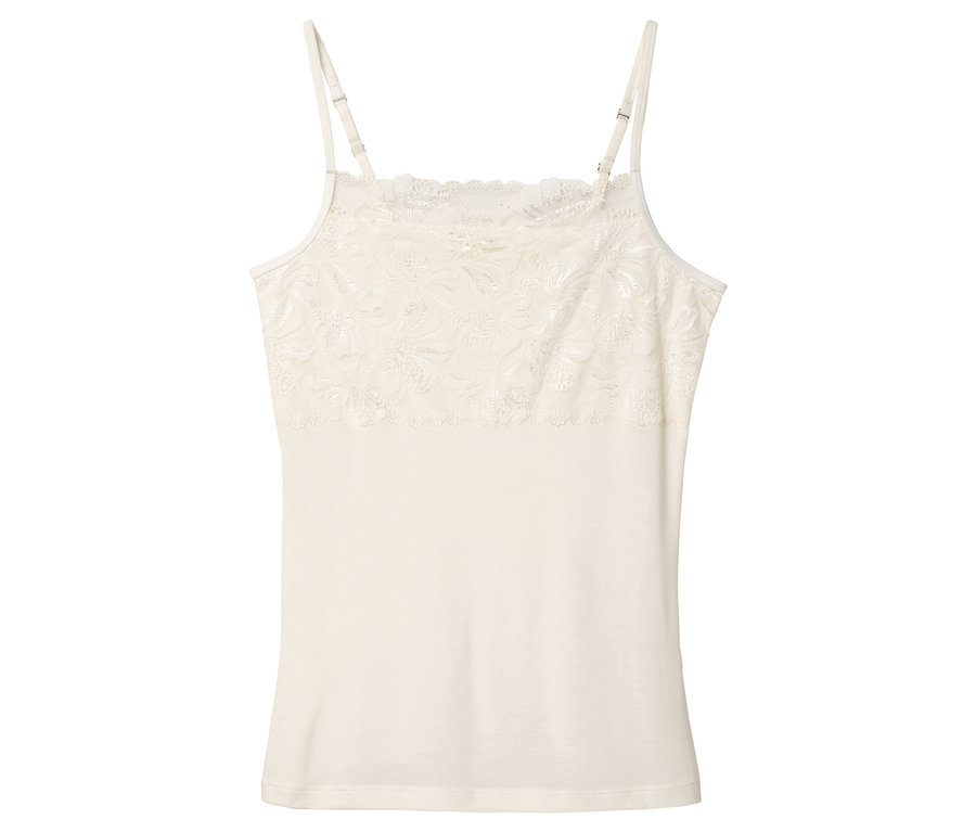 Na bílém pozadí leží krémové tílko s krajkou.