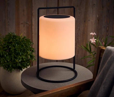 Svítící lampa s černým rámem stojí venku na šedém stole.