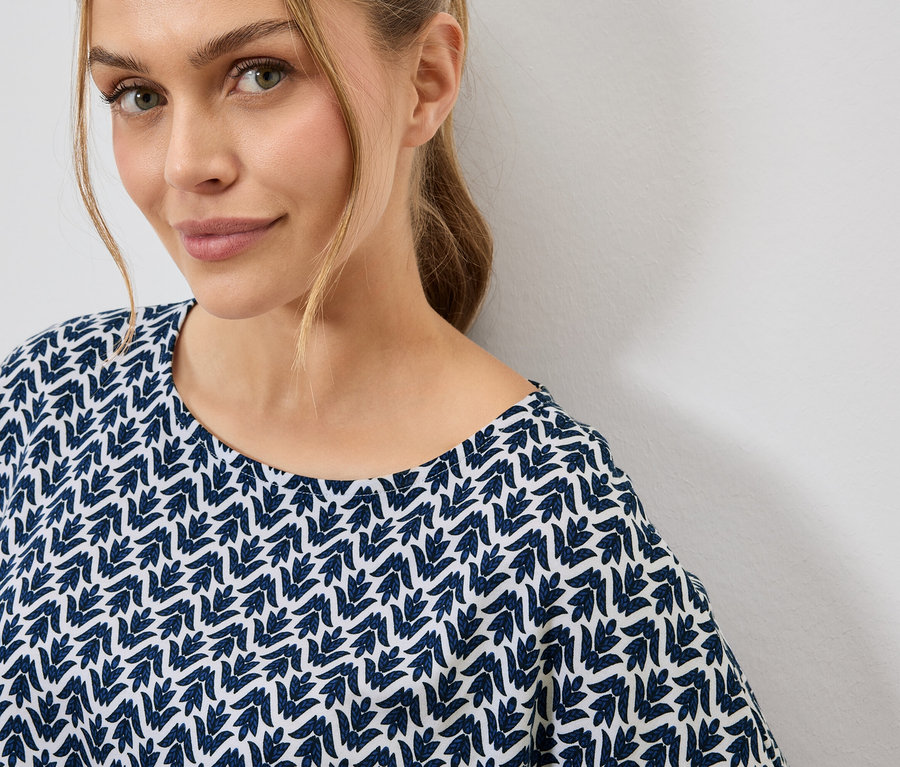 Portrét blondýny v modro-bílém topu se vzorem listů.