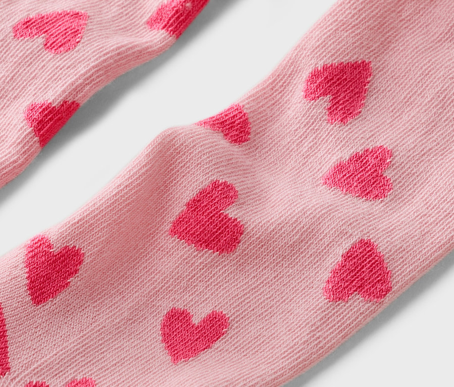 Detailní záběr na světle růžové ponožky s červeným vzorem srdíček.