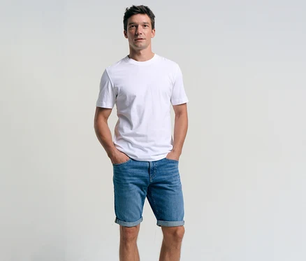 Muž v bílém tričku a džínových šortkách Tom Tailor TTJOSH REGULAR SLIM, mid stone bright blue denim, s rukama v kapsách.