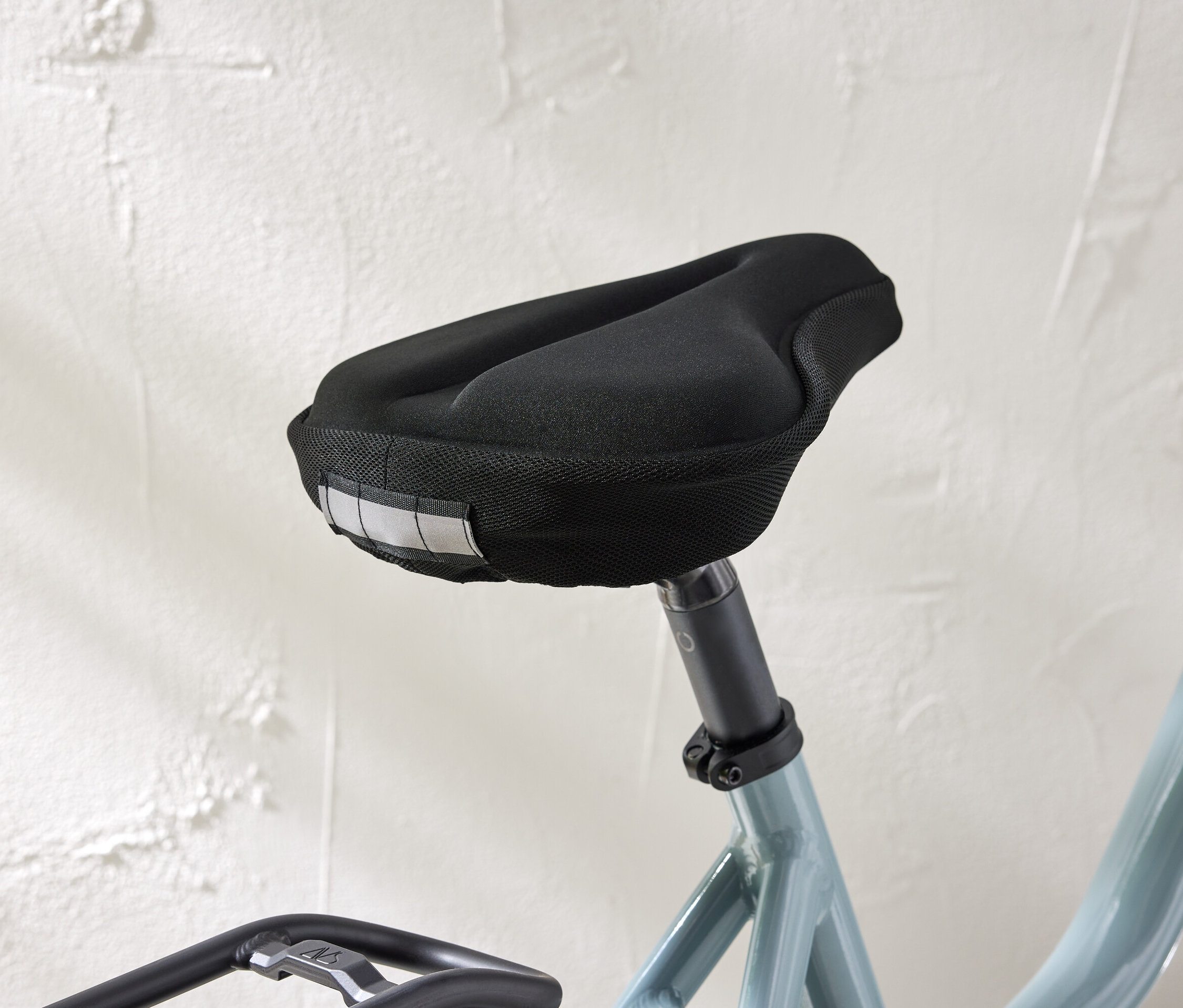 Detailní záběr sedla na kolo s černým potahem a reflexními proužky na bílém pozadí stěny.