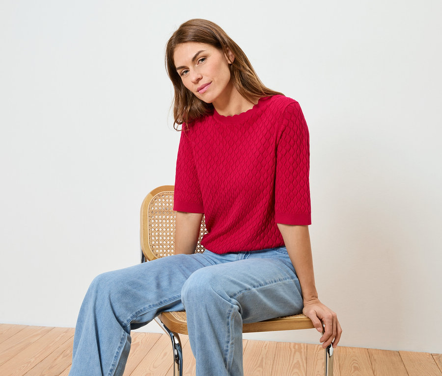 Žena sedí na židli a má na sobě červený top a džíny.