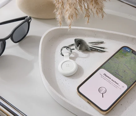 Na podnosu leží sluneční brýle, klíče, bílý tracker a smartphone s mapovou aplikací.