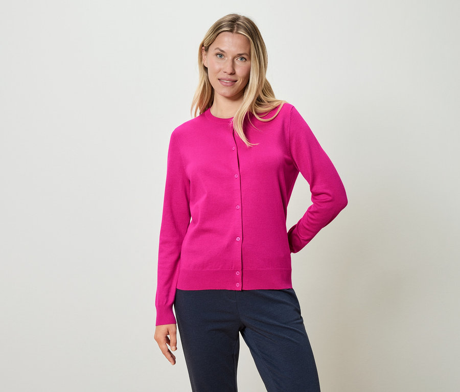 Žena má na sobě růžový kardigan a modré kalhoty.