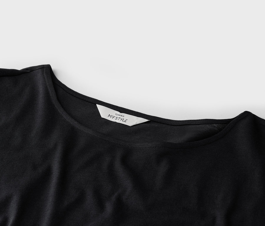 Detailní záběr na černé tričko s bílou etiketou 'TCHIBO MY STYLE' na límci.