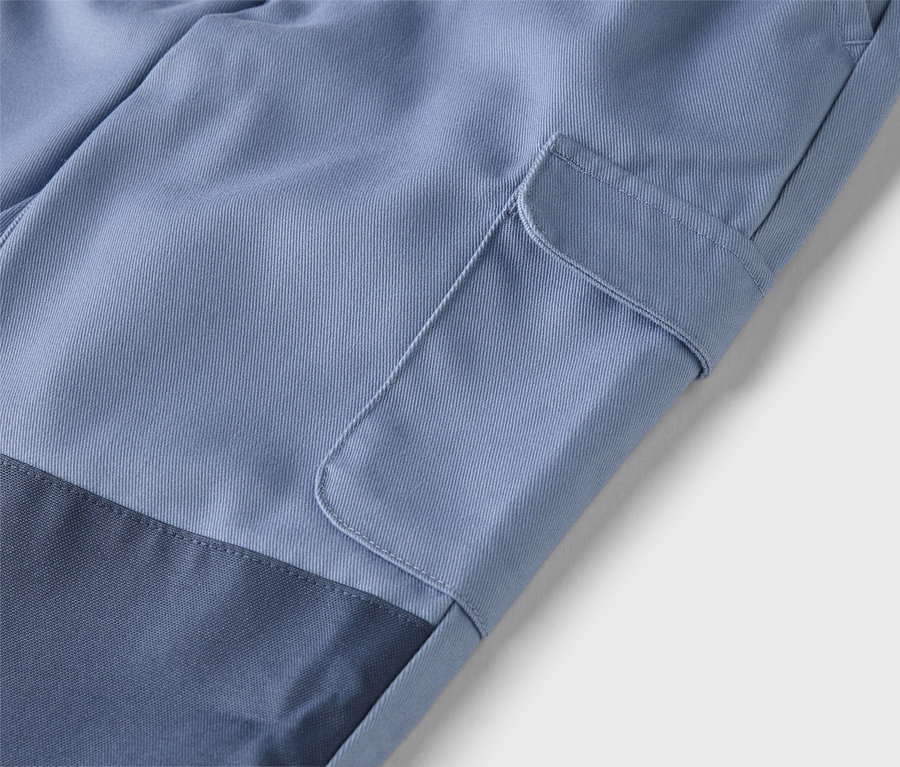 Detailní záběr světle modrých kalhot s našitou kapsou na nohavici a tmavě modrou vsadkou na spodní části nohavice.