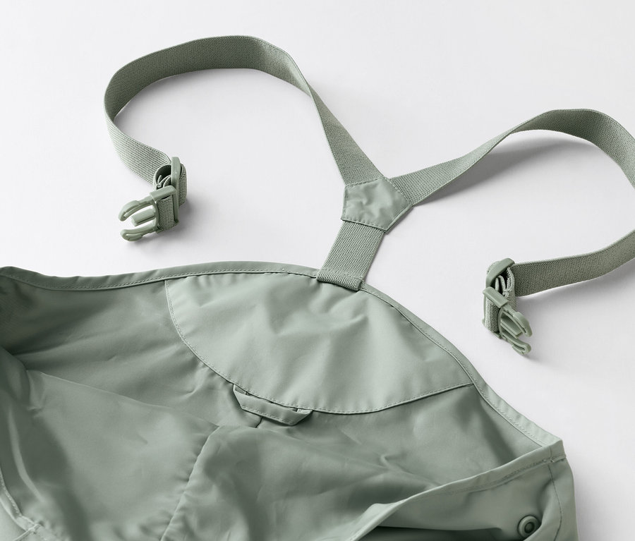 Detailní záběr na zelené nepromokavé kalhoty s laclem a přezkami na bílém pozadí.