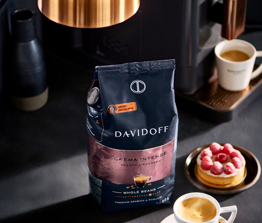 Balíček DAVIDOFF CAFÉ Crema Intense 1000 g zrnkové kávy stojí vedle šálku kávy a malinového koláče.