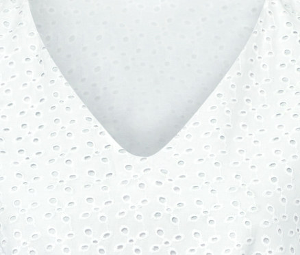 Detail bílých šatů s ažurovou výšivkou.