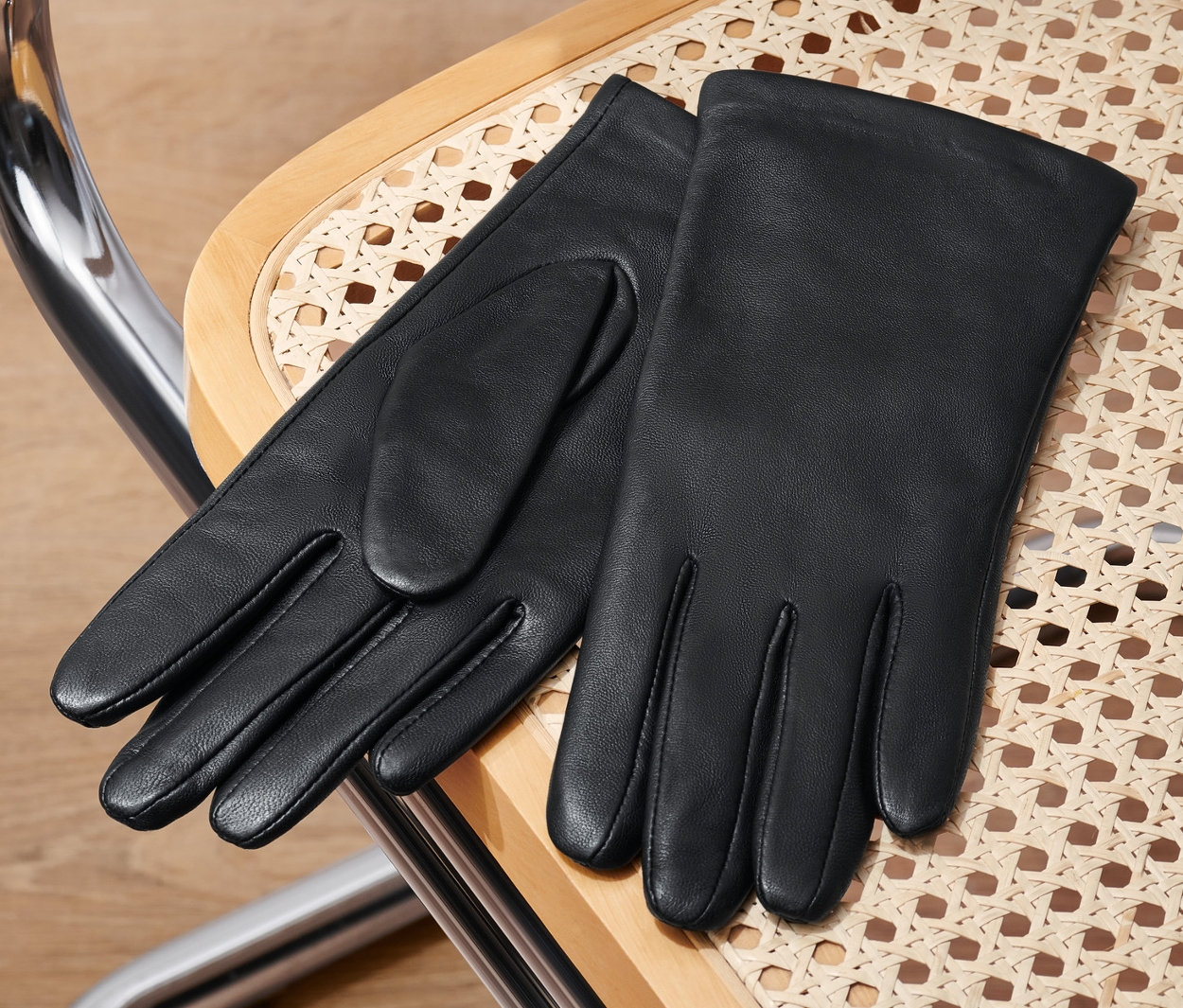 Černé kožené rukavice leží na proutěné židli.