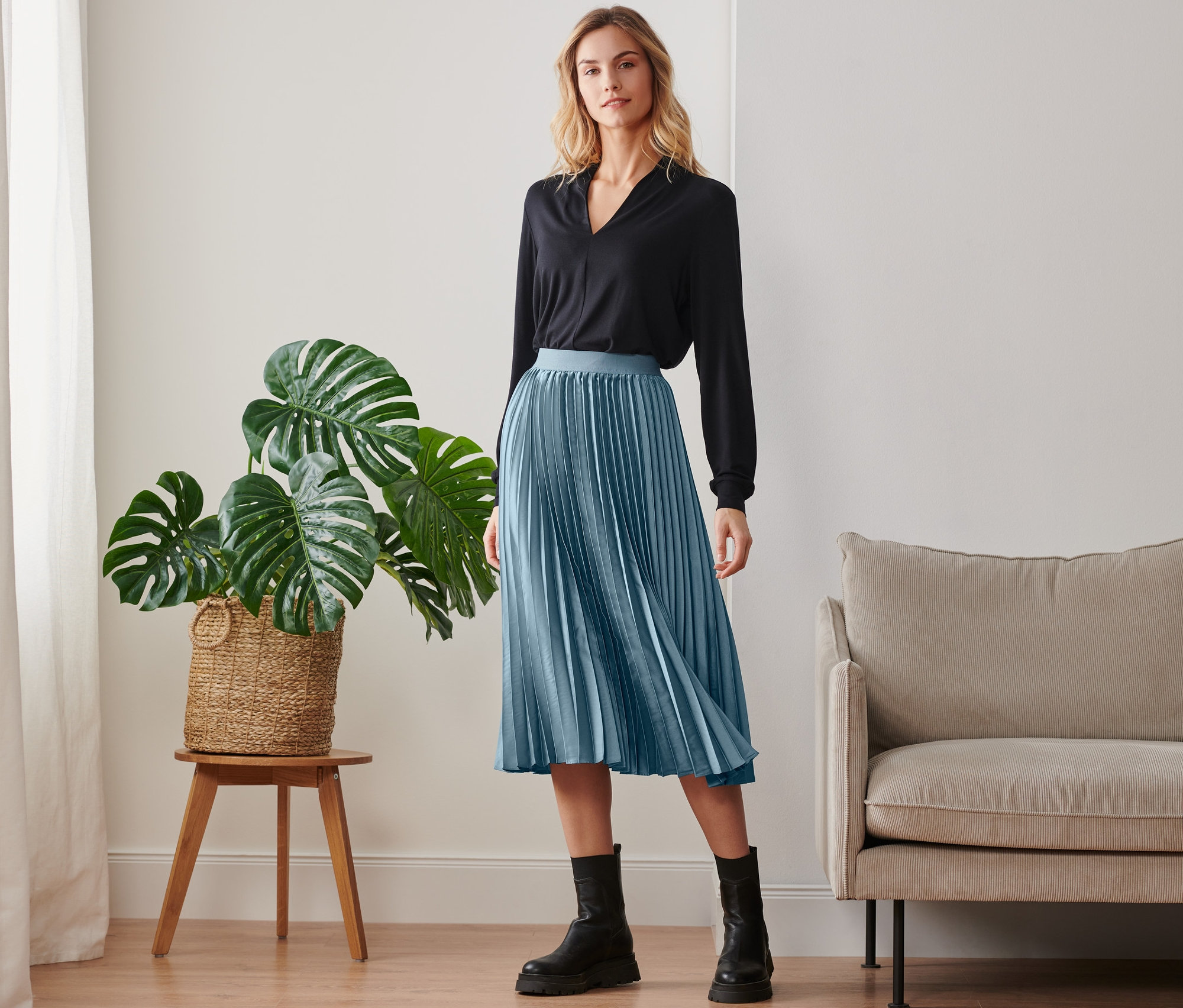 Žena pózuje v černém topu a plisované sukni.