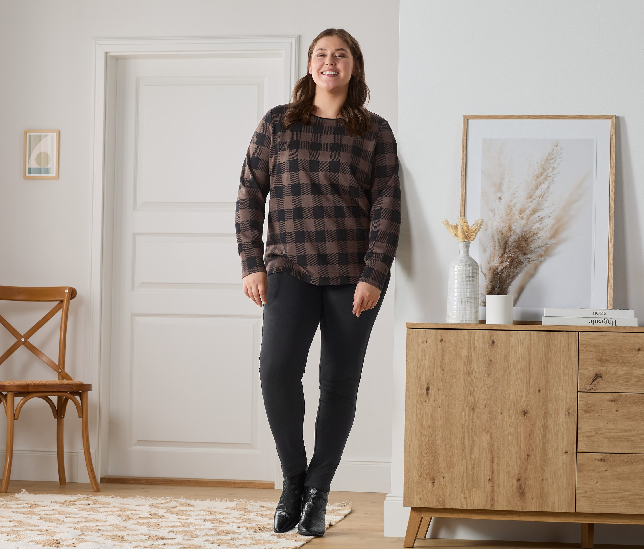 Žena pózuje v džegínách a kostkované mikině.