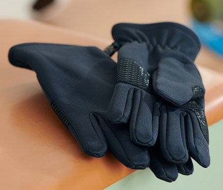 Dvoje softshellové rukavice leží na malé stolici. V pozadí je fotbalový míč a skateboard.