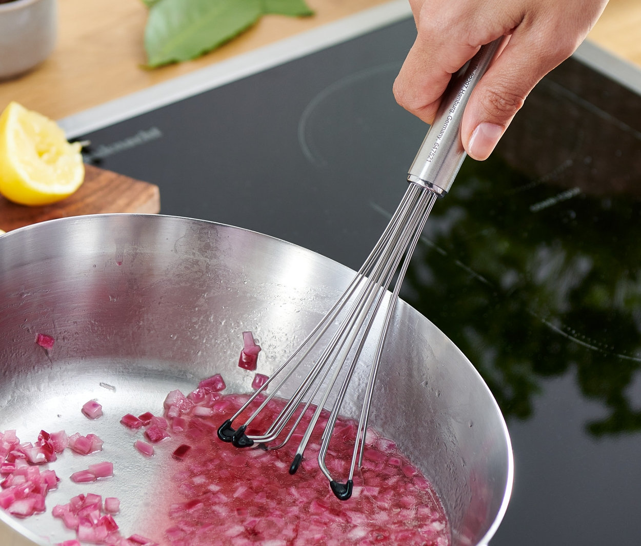 Ruka míchá profi metlou nakrájenou červenou cibuli v hrnci na sporáku.