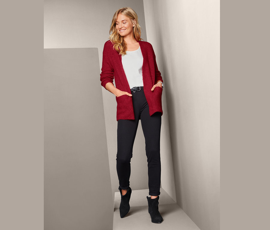 Žena pózuje v pleteném kardiganu, černých kalhotách a botách.