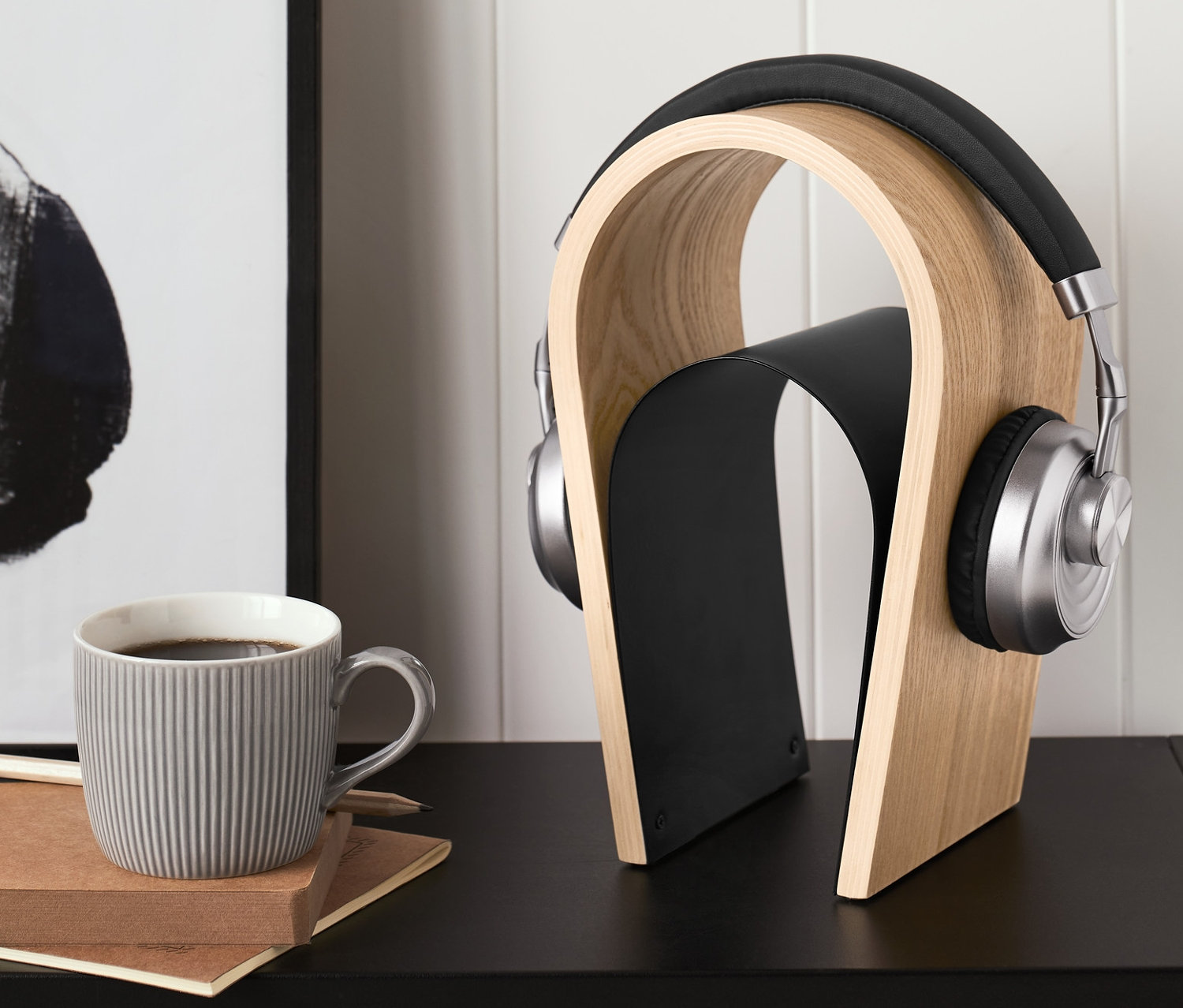 Sluchátka na dřevěném stojanu na sluchátka. Vedle nich stojí šedý hrnek a leží zápisník.