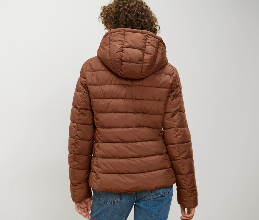 Žena zezadu má na sobě koňakovou prošívanou bundu s kapucí.
