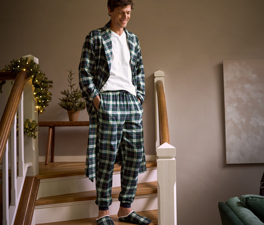Muž schází po schodech v kostkovaném flanelovém županu, flanelových kalhotách, pantoflích a tričku s výstřihem do V.