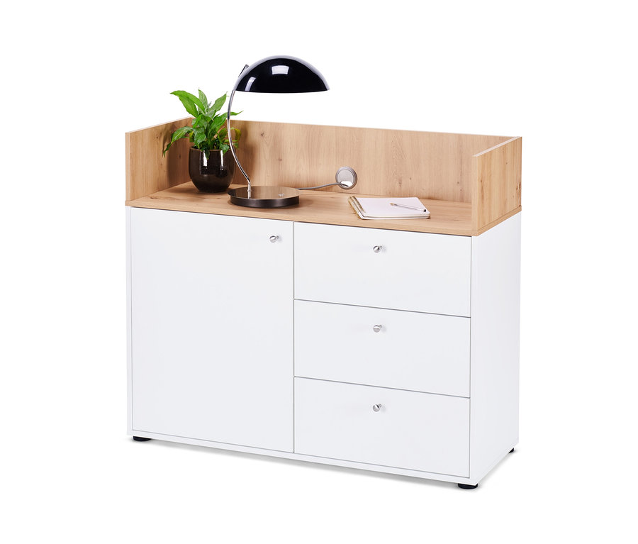 Bílá komoda se zásuvkami a dvířky s rostlinou v květináči, lampou a zápisníkem nahoře.