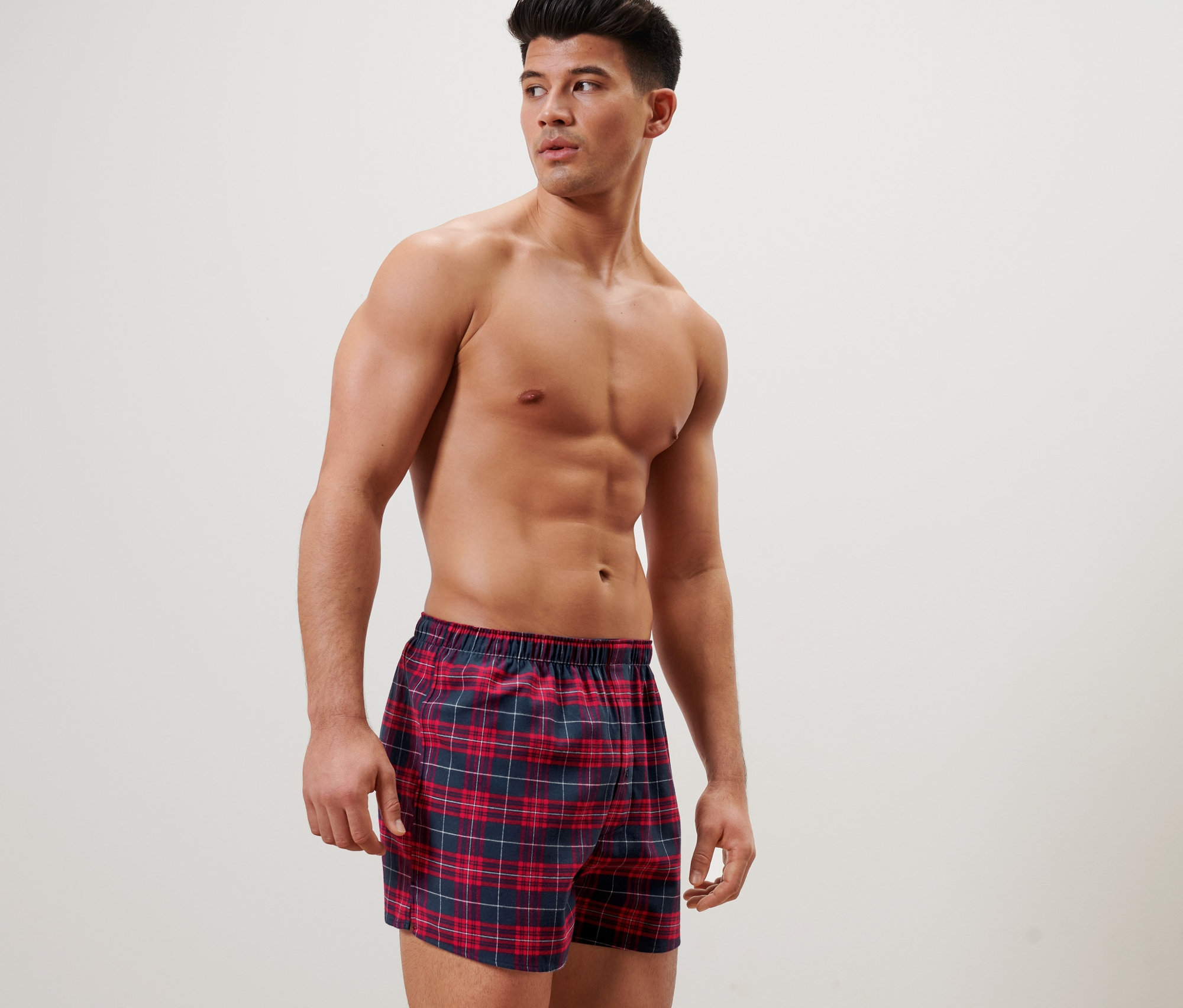 Muž pózuje v kostkovaných flanelových boxerkách.