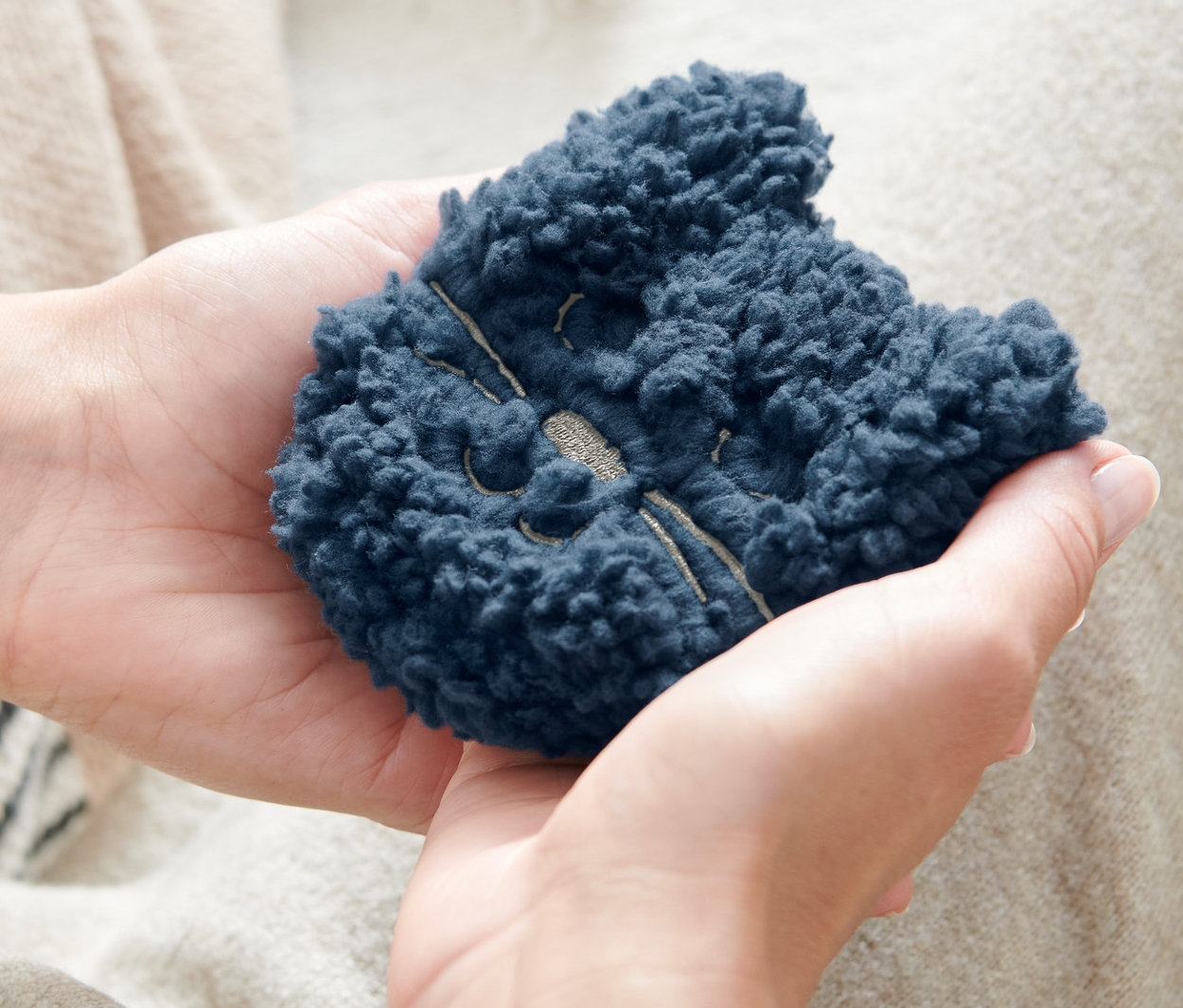 Osoba drží v rukou dva hřejivé polštářky do kapsy »Kočka«.