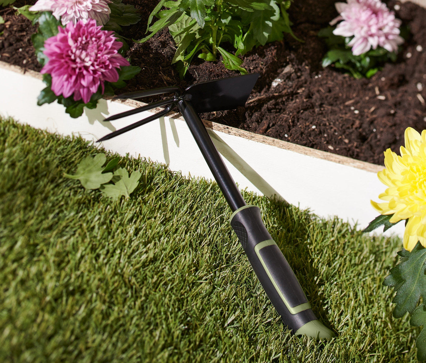 Černá dvojitá zahradní motyčka leží na trávě vedle květináče s žlutými květy.