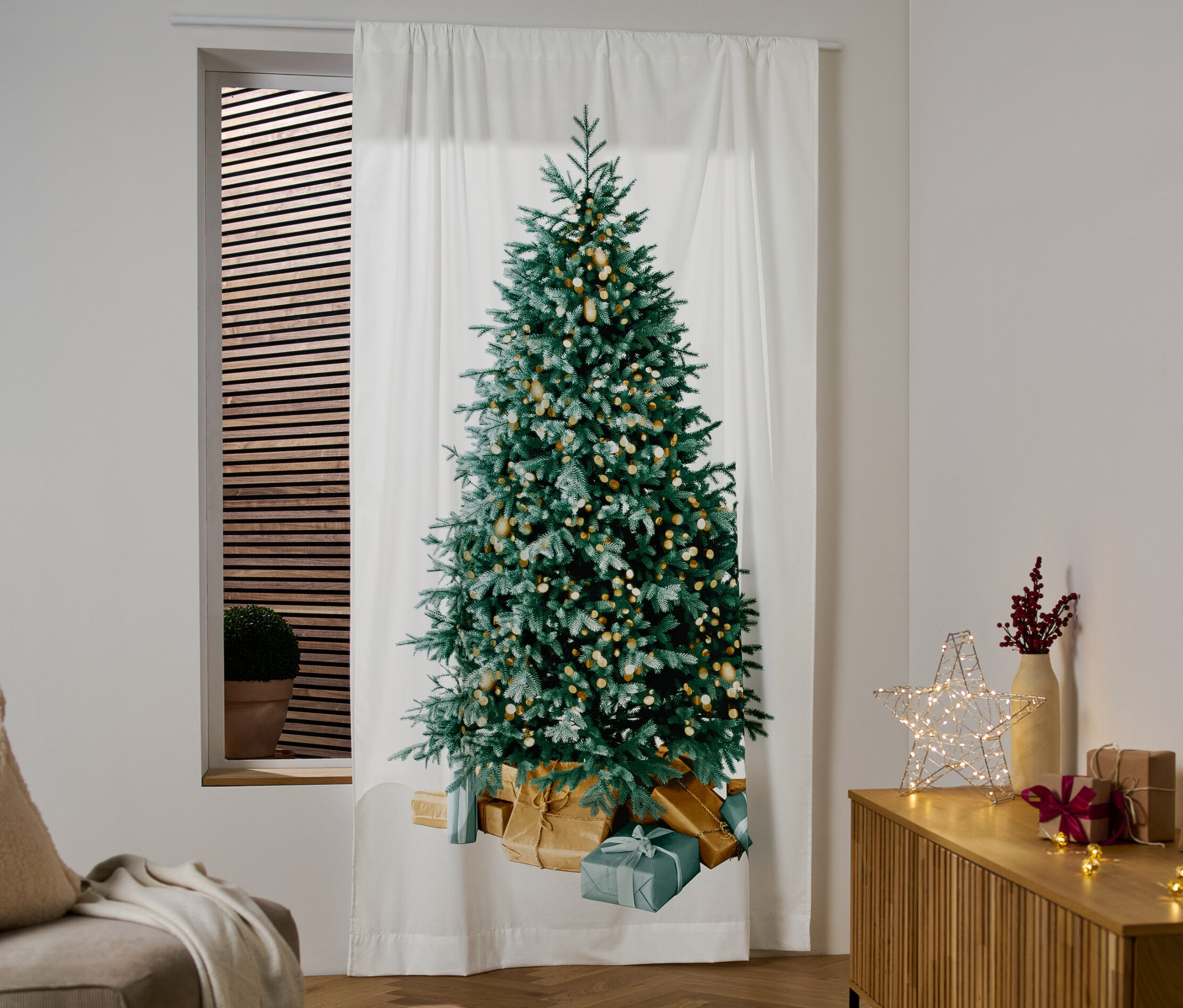 Bílý závěs s motivem vánočního stromku visí v okně.