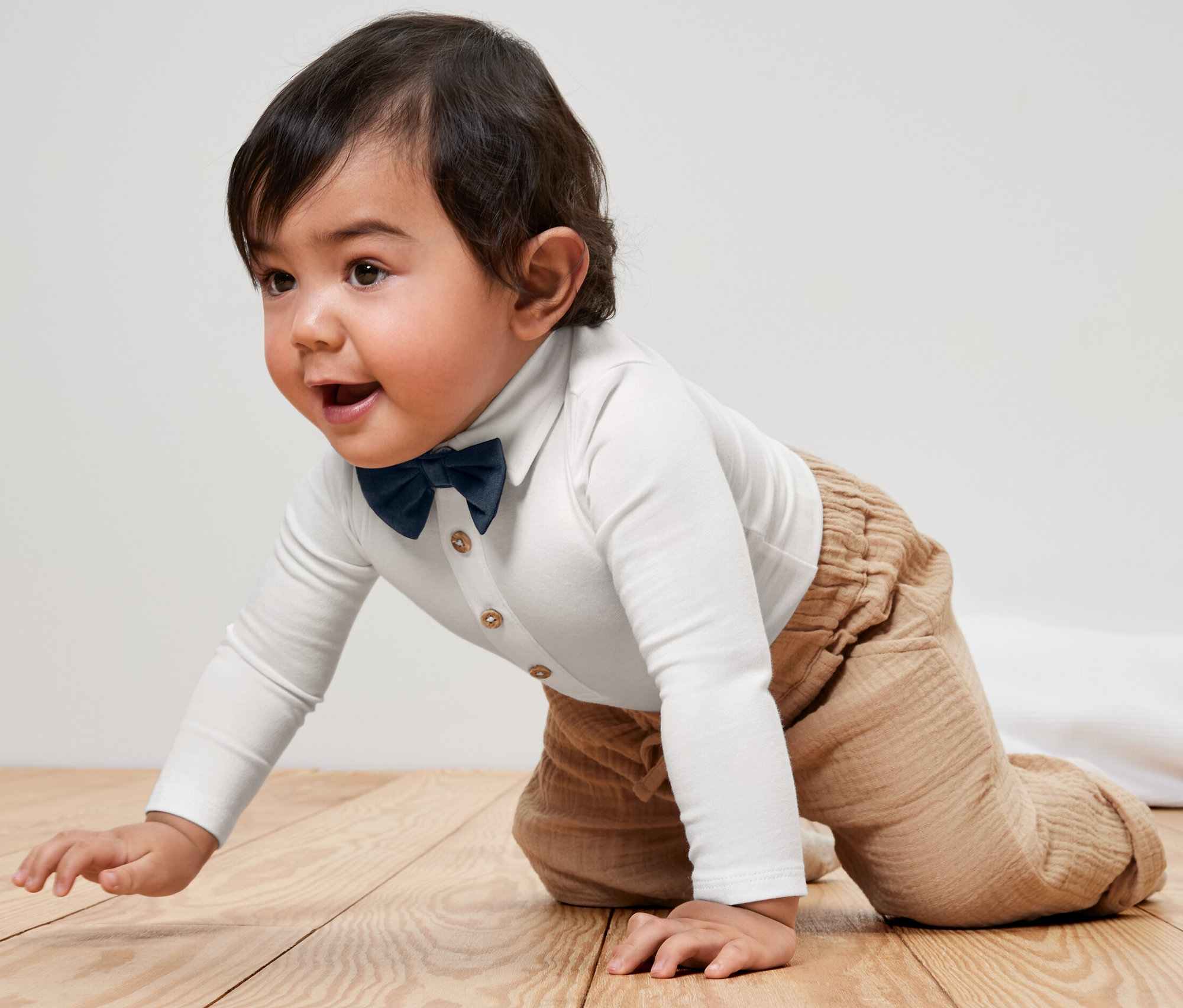 Kojenecké body s motýlkem, lezoucí na dřevěné podlaze.