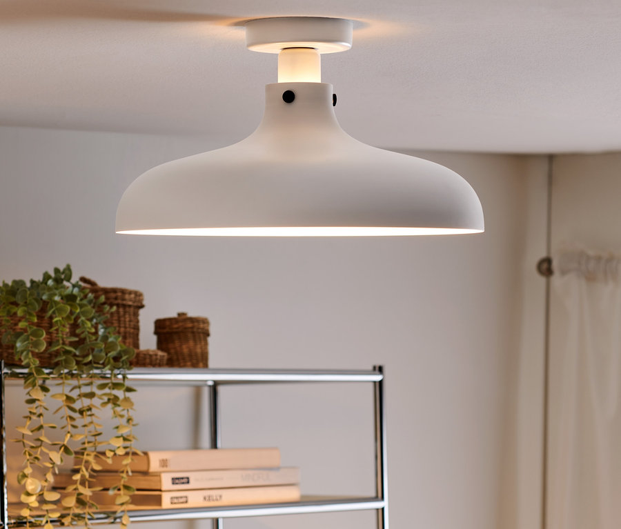 Kovové závěsné stropní svítidlo nad policí s rostlinami a knihami.